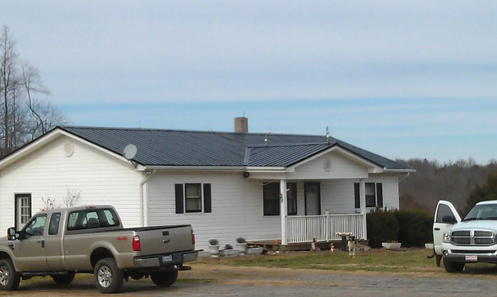 Finished dark metal roof on a white ranch home with work trucks parked in La Crosse